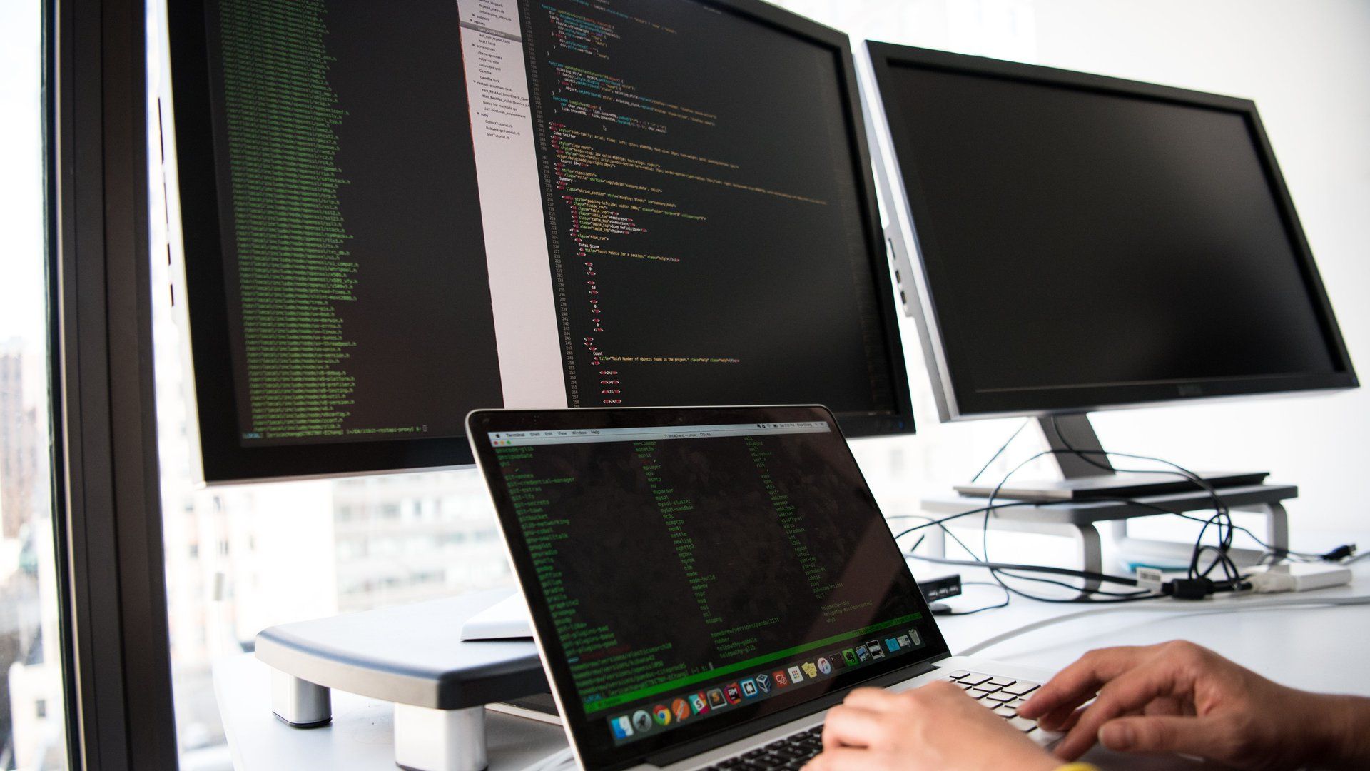 A developer working across multiple monitors and a laptop, each showing a different piece of code